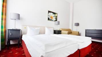 Habitación de hotel con una cama grande, dos mesitas de noche, un sillón y un cuadro en la pared.
