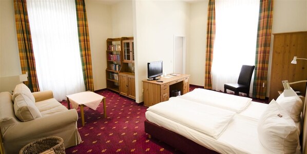 Habitación de hotel con cama, escritorio, computadora, estantería, sillón y sofá.