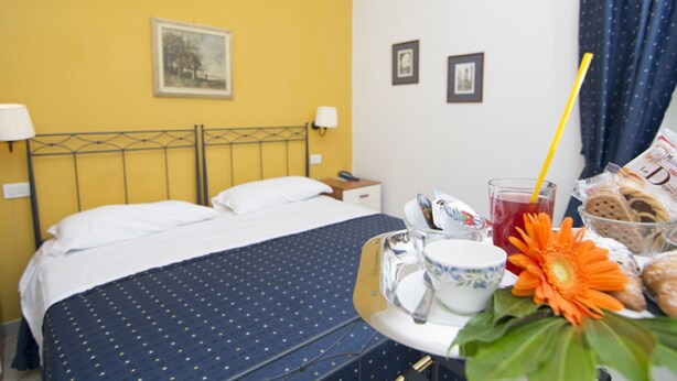 A hotel room with a bed, bedside tables, a small table with breakfast items, and a window with curtains. - Villa Margherita (Naples)