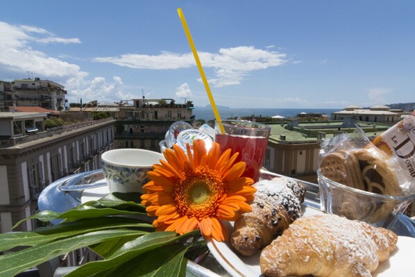 A table with pastries, a flower, a drink, and a cup, overlooking a cityscape with buildings and a clear sky. - Villa Margherita (Naples)