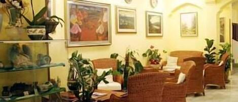 A lobby with wicker furniture, potted plants, and framed artwork on the walls.