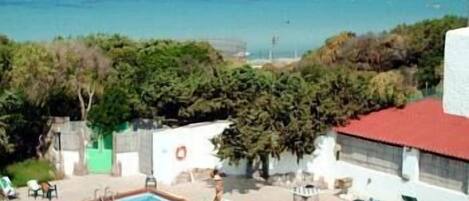Una piscina con gente, un edificio de techo rojo y vistas al mar.