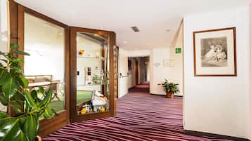 Un couloir d’hôtel avec un tapis à rayures zébrées, des portes en verre encadrées de bois, un comptoir de réception et une œuvre d’art encadrée accrochée au mur.