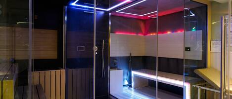 A glass-walled sauna with a wooden bench and a control panel.