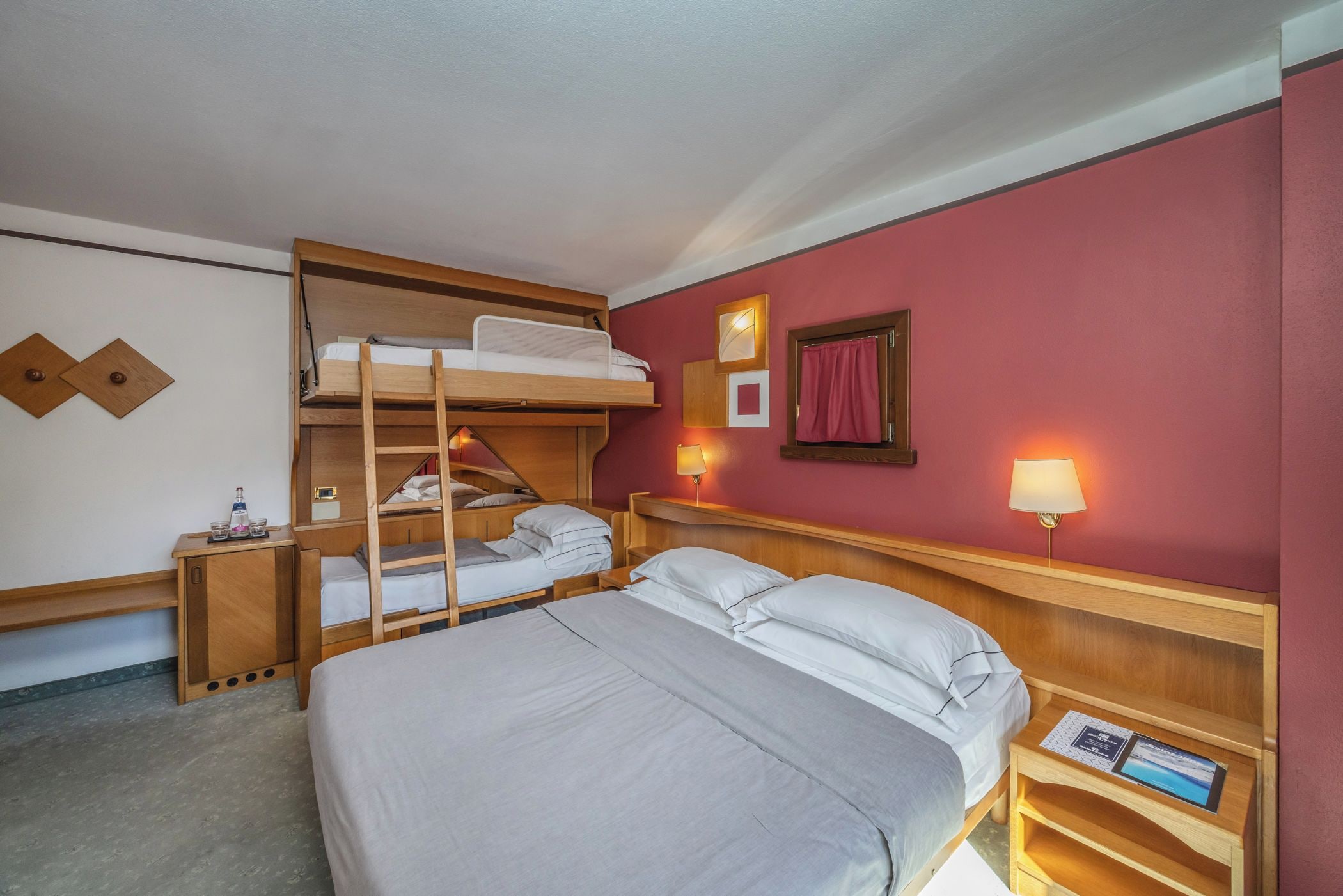 Una habitación de hotel con literas, un escritorio, una mesita de noche y una lámpara.
