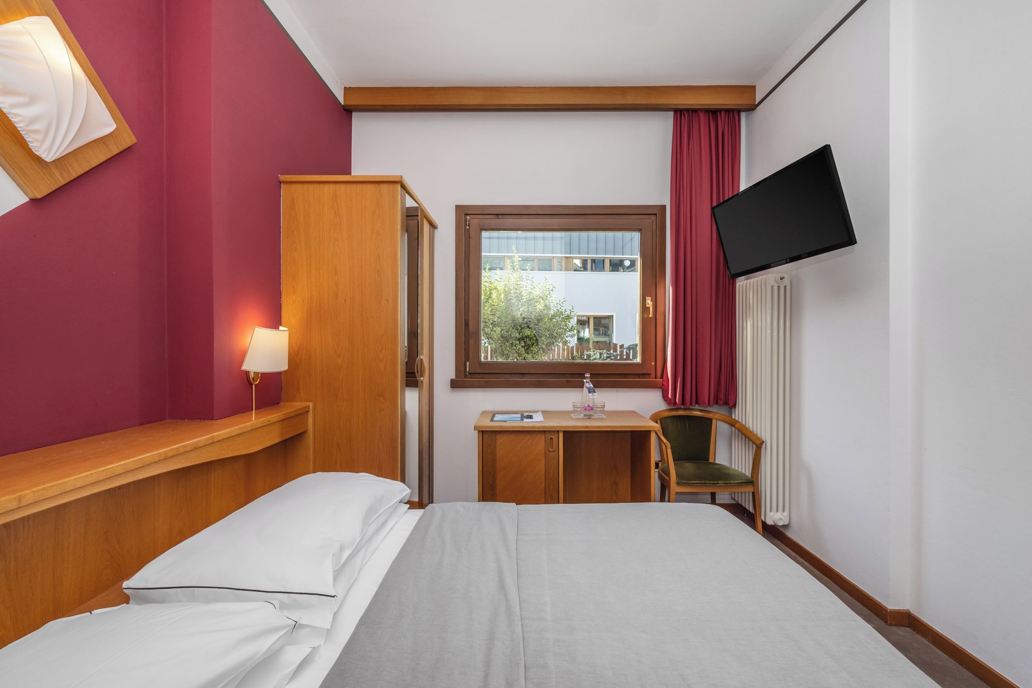 Habitación de hotel con cama, escritorio, silla, televisión y ventana con vista a un edificio.