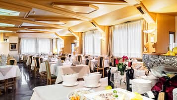 A spacious dining area with multiple tables set for a meal, featuring a variety of dishes and wine bottles.