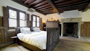 Um quarto tradicional com uma cama grande, vigas de madeira, lareira e janela com um padrão de treliça.