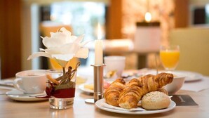 A breakfast setting with croissants, a cup of coffee, a glass of orange juice, and a candle. - Citta Trüffel Hotel (Wiesbaden)