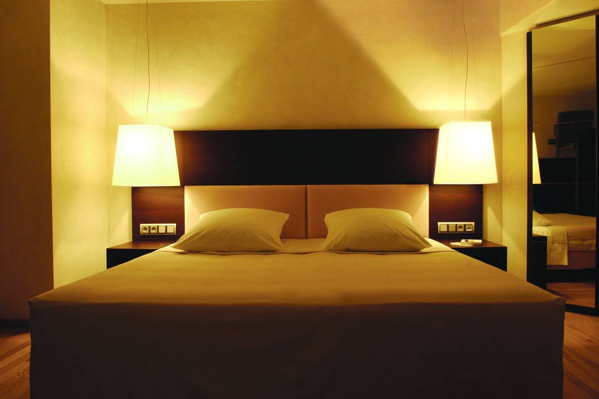 A hotel room with a large bed, two bedside lamps, and a nightstand with a phone and a small table.