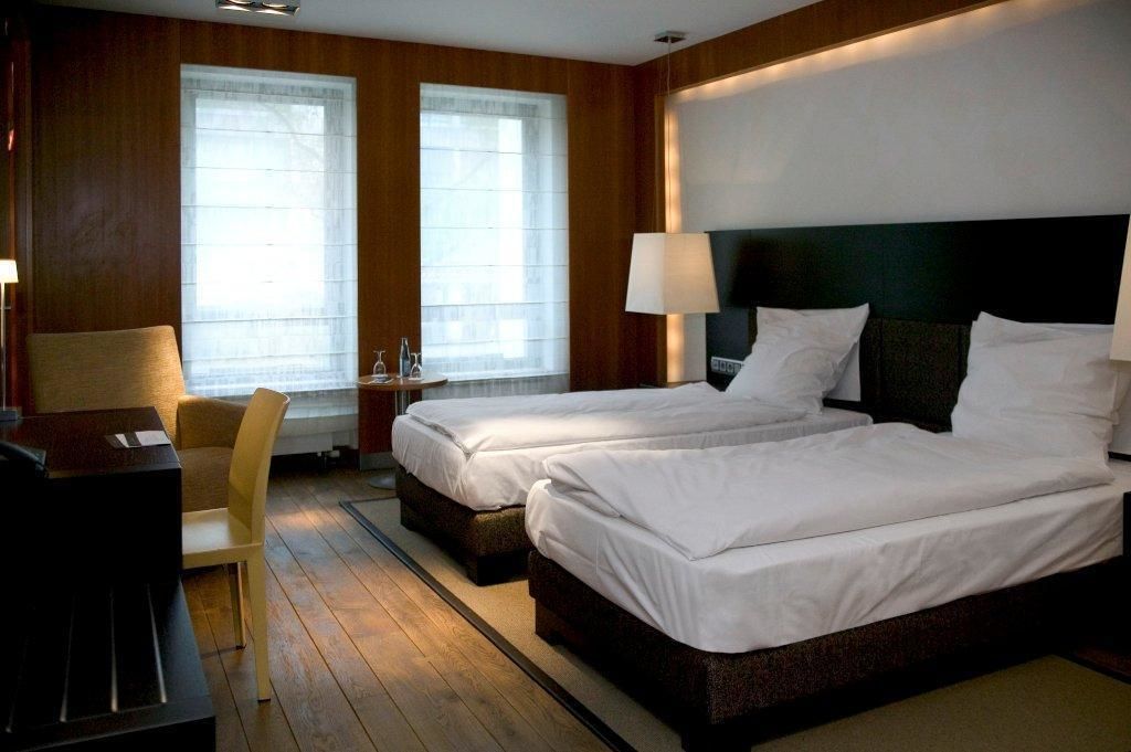 Ein Hotelzimmer mit zwei Betten, einem Schreibtisch, einem Stuhl und einem Fenster mit Jalousien.