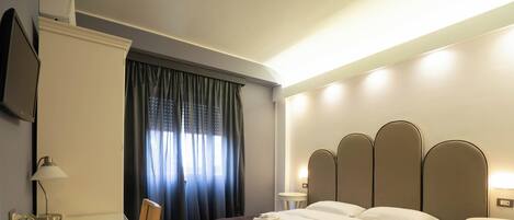 Una habitación de hotel con cama, mesitas de noche, escritorio, silla, televisor y ventana con cortinas.