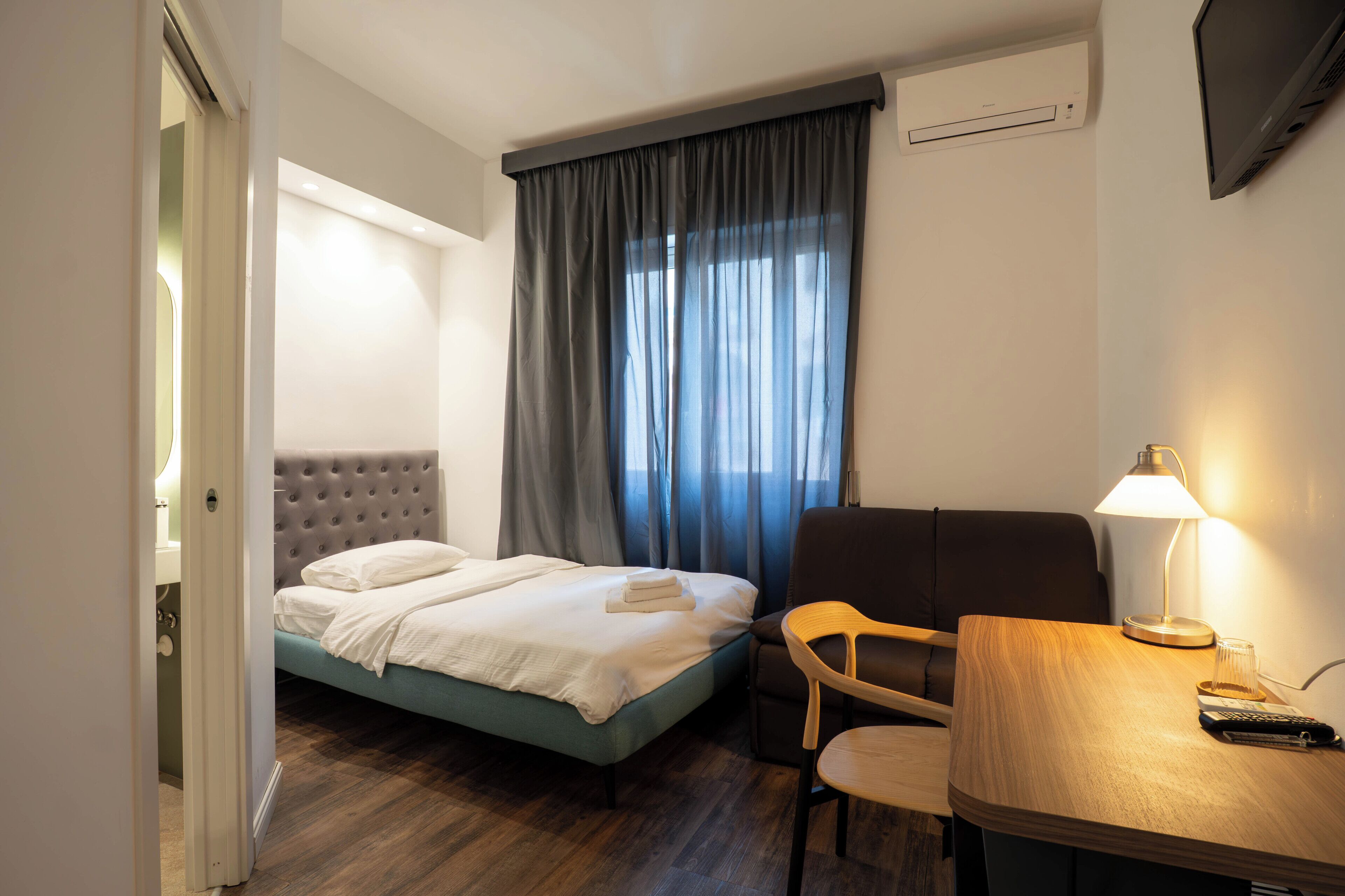 Une chambre d’hôtel avec un lit, un bureau avec une lampe, une chaise et un téléviseur fixé au mur.