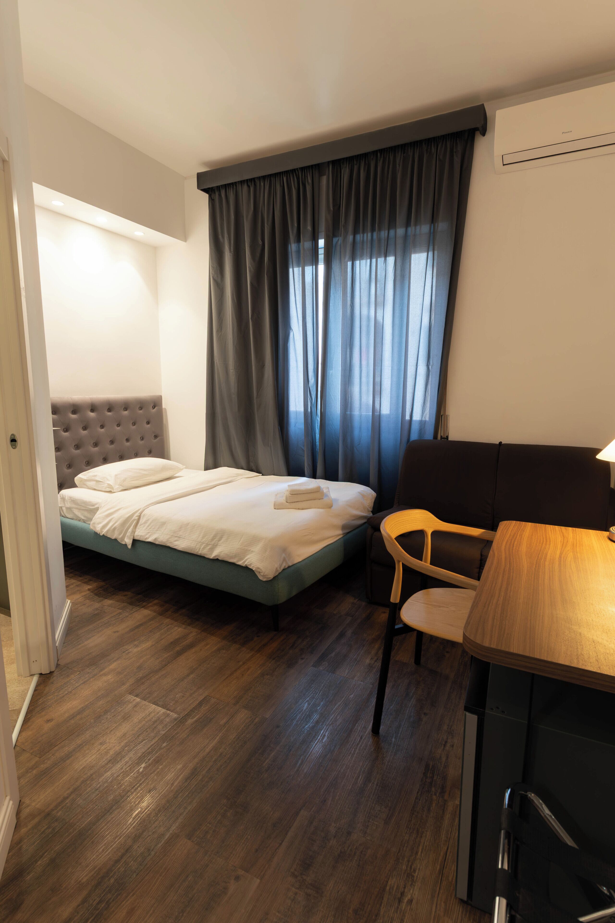 A hotel room with a bed, a desk, a chair, and a window with curtains.