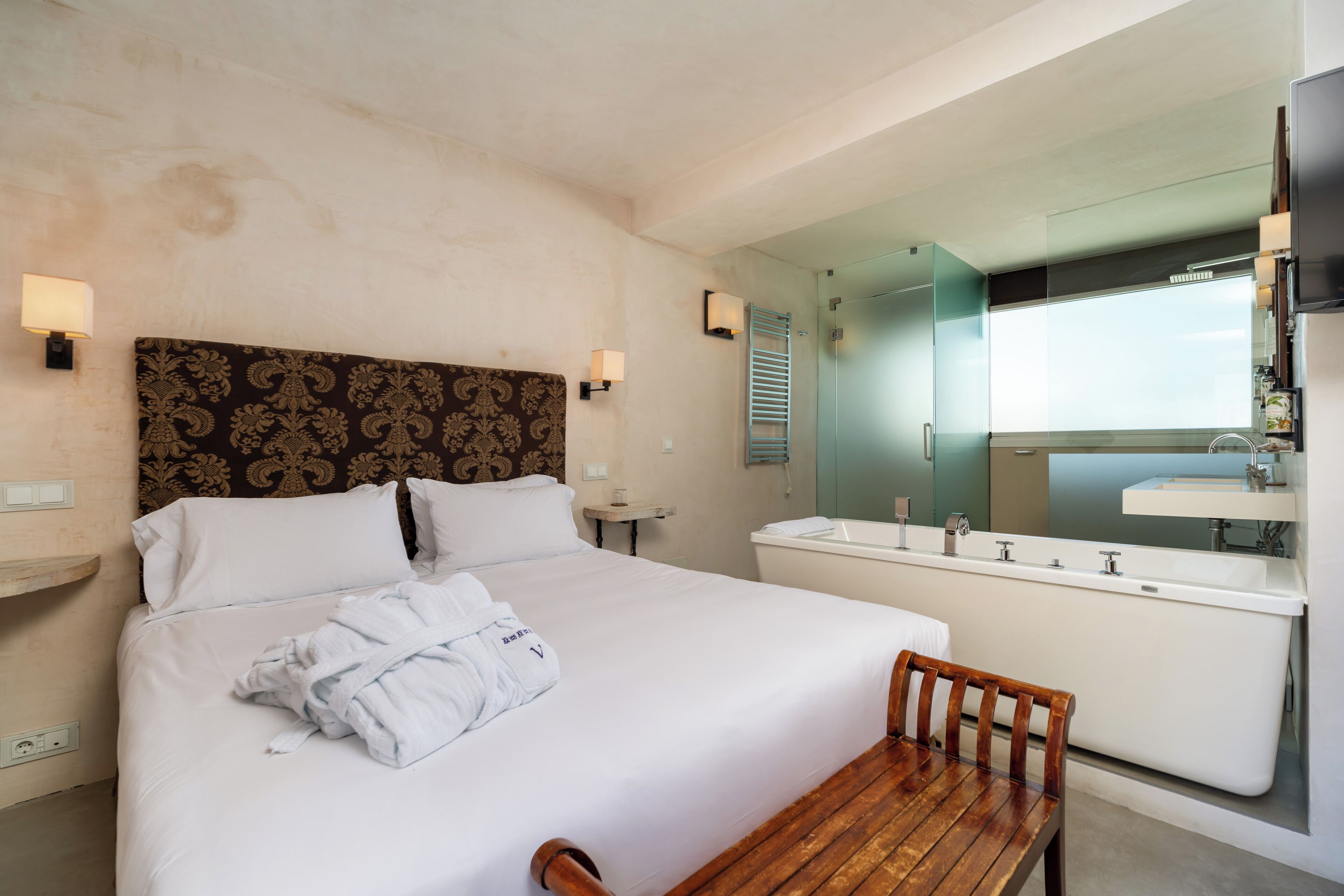 A hotel room with a large bed, a wooden chair, a bathroom with a bathtub, and a mirror.
