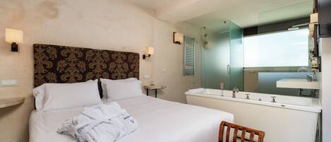 Ein Hotelzimmer mit einem großen Bett, einem Holzstuhl, einem Badezimmer mit Badewanne und einem Spiegel.