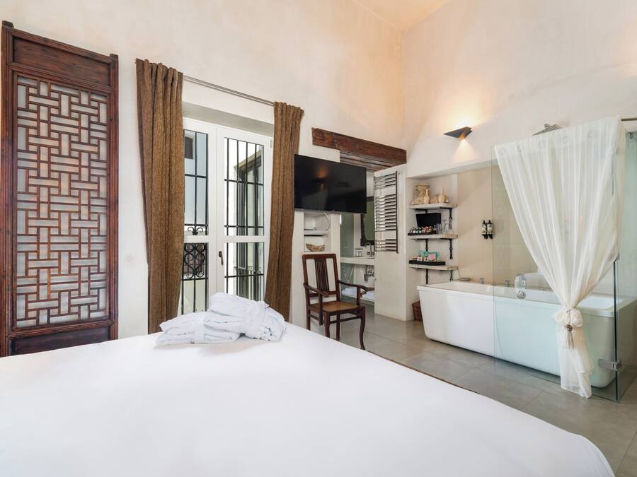 A hotel room with a bed, a chair, a TV, a bathroom with a shower curtain, and a large window.