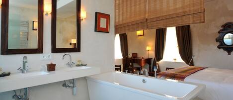 A bathroom with a bathtub, two sinks, a mirror, and a window with curtains.