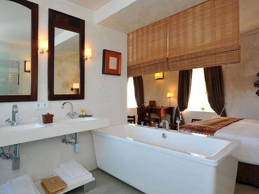 A bathroom with a bathtub, two sinks, a mirror, and a window with curtains.