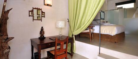 A hotel room with a wooden desk, a chair, a lamp, a mirror, and a bed.