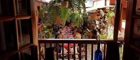 An outdoor dining area with tables and chairs, surrounded by potted plants and a view of buildings.