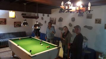 A pool table in a room with a wooden ceiling, stone wall decorations, and a hanging light fixture.