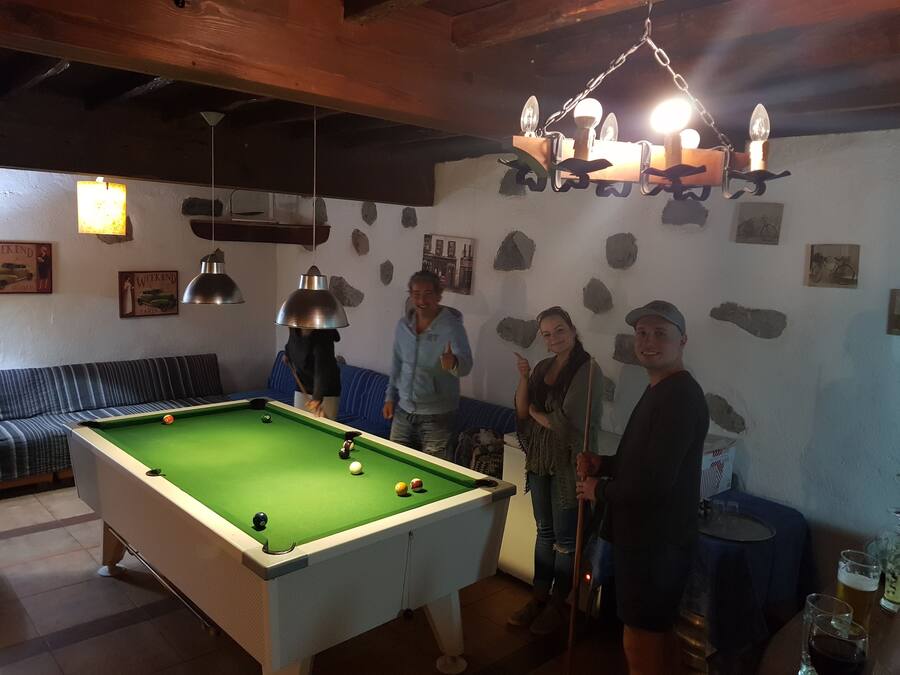 A pool table in a room with a wooden ceiling, stone wall decorations, and a hanging light fixture.