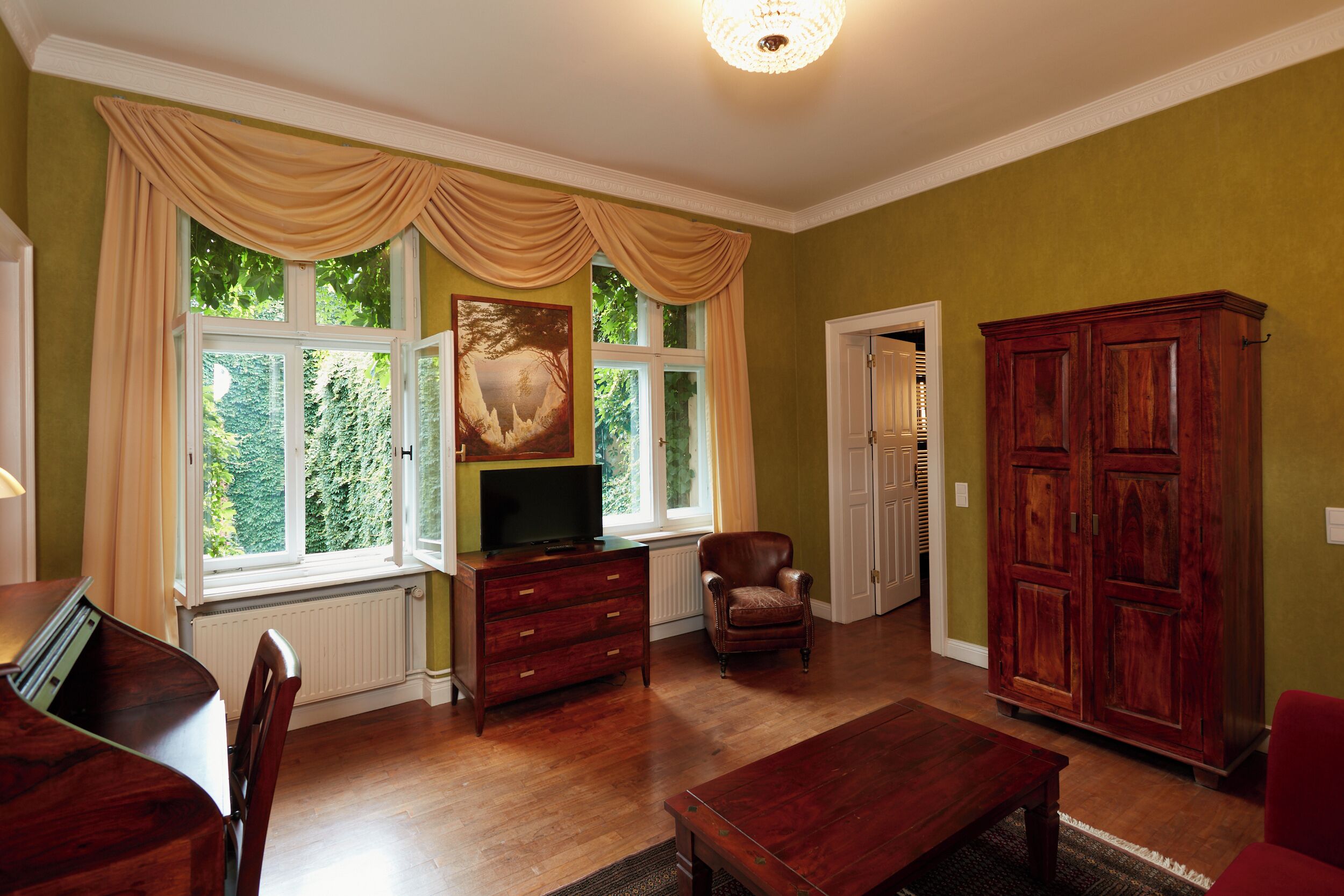 A spacious living room with a large window, a television, a wooden cabinet, and a dining area with a table and chairs.