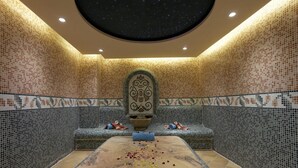 Une pièce dotée d’un plafond étoilé, de murs décorés de motifs, d’un espace de détente central agrémenté de coussins et d’un sol en marbre.