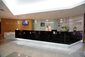 A modern reception desk with a marble base and black top, a flat-screen TV mounted on the wall, and a receptionist standing behind it.