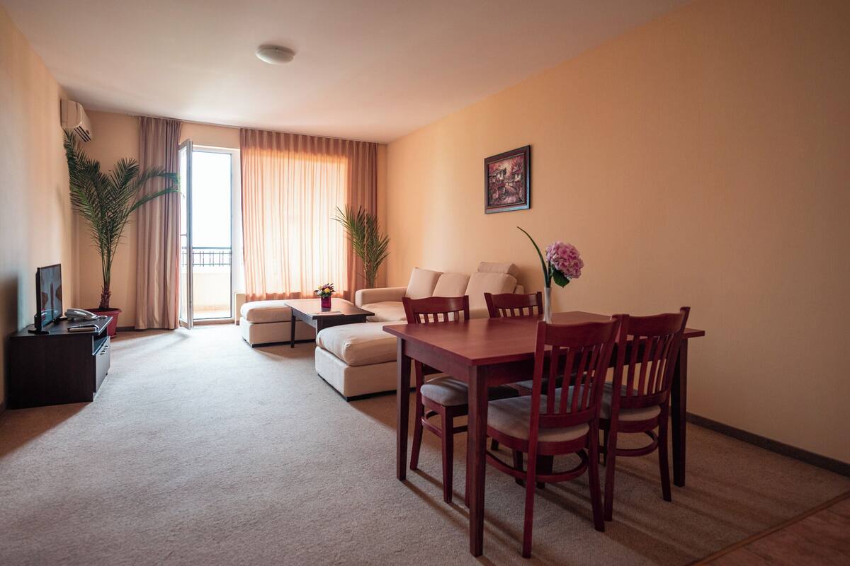 A living room with a sofa, a dining table with chairs, a TV, and a plant.