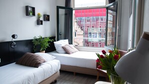 A modern hotel room with two beds, a large window, and a view of buildings outside. - La Boheme (Amsterdam)