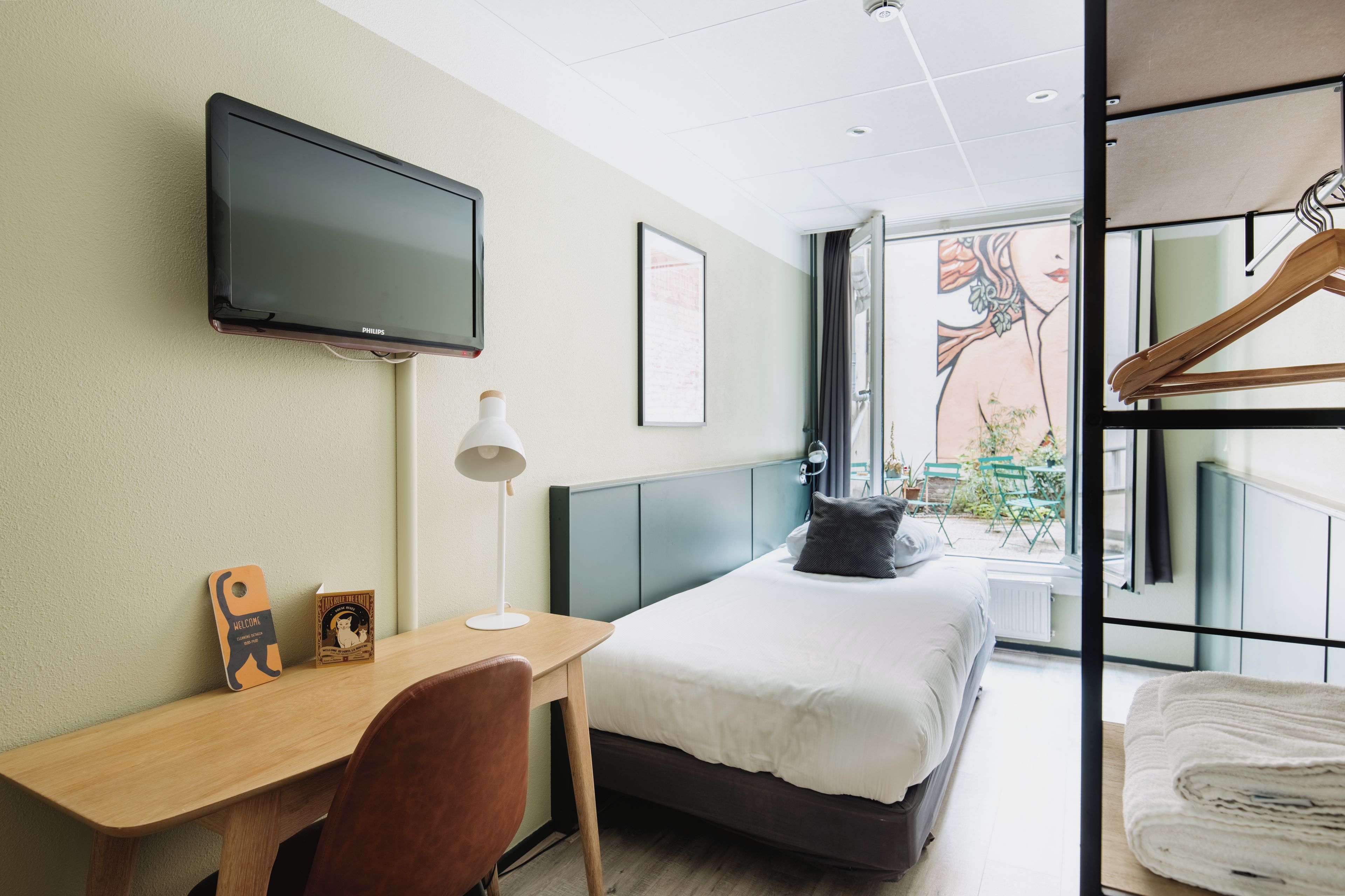 A hotel room with a bed, a desk, a chair, a television, and a window with a view of the outside.