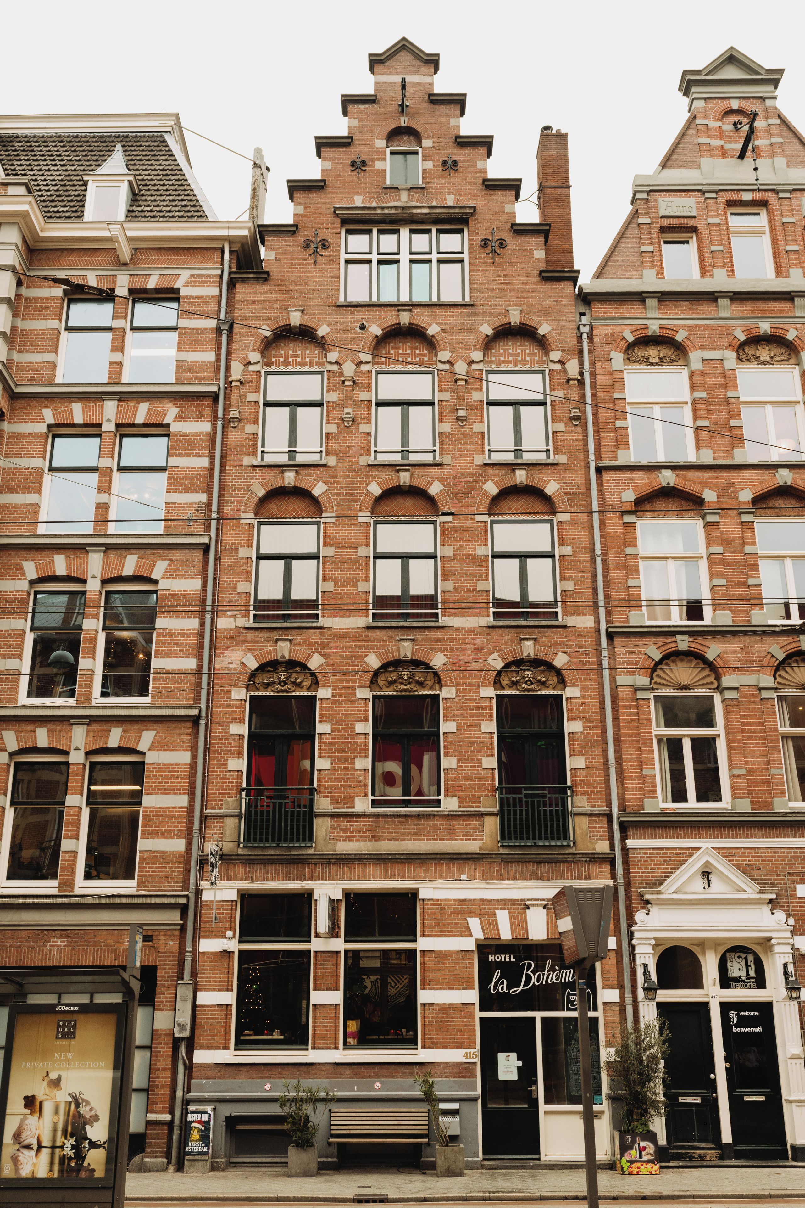 A multi-story building with a traditional brick facade, large windows, and a ground-floor entrance with a bench and a sign for a hotel.
