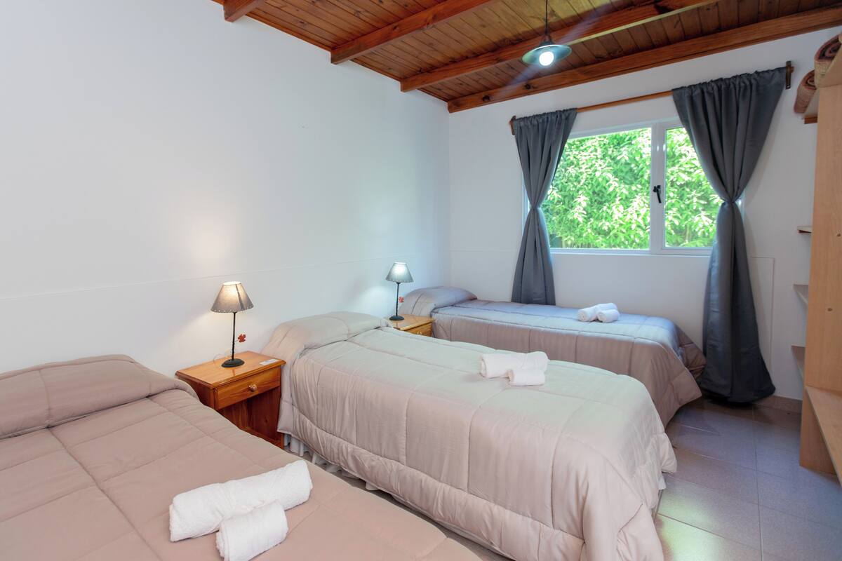 Une chambre avec deux lits, une table de chevet avec une lampe, une fenêtre avec des rideaux et un plafond en bois.