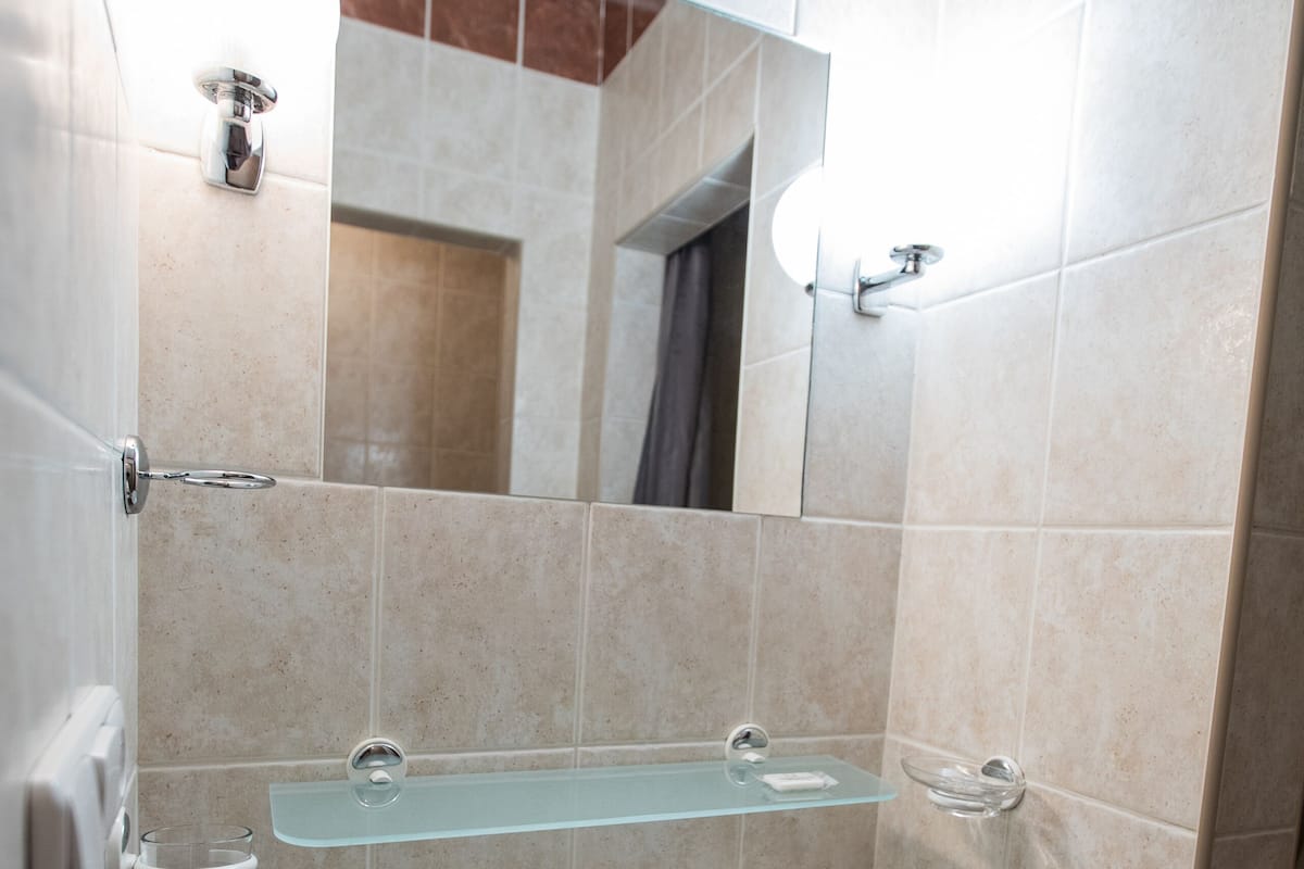 Une salle de bain avec un lavabo blanc, une étagère en verre et un miroir au-dessus.