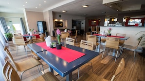 Un comedor moderno con sillas y mesas de madera, una barra con un tapete rojo y plantas en macetas.