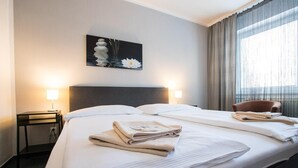 Habitación de hotel con una cama grande, dos lámparas de noche, una silla y un cuadro en la pared.