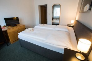 A hotel room with a bed, a desk with a television, a mirror, and a bedside lamp. - A-Sport Hotel (Brno)
