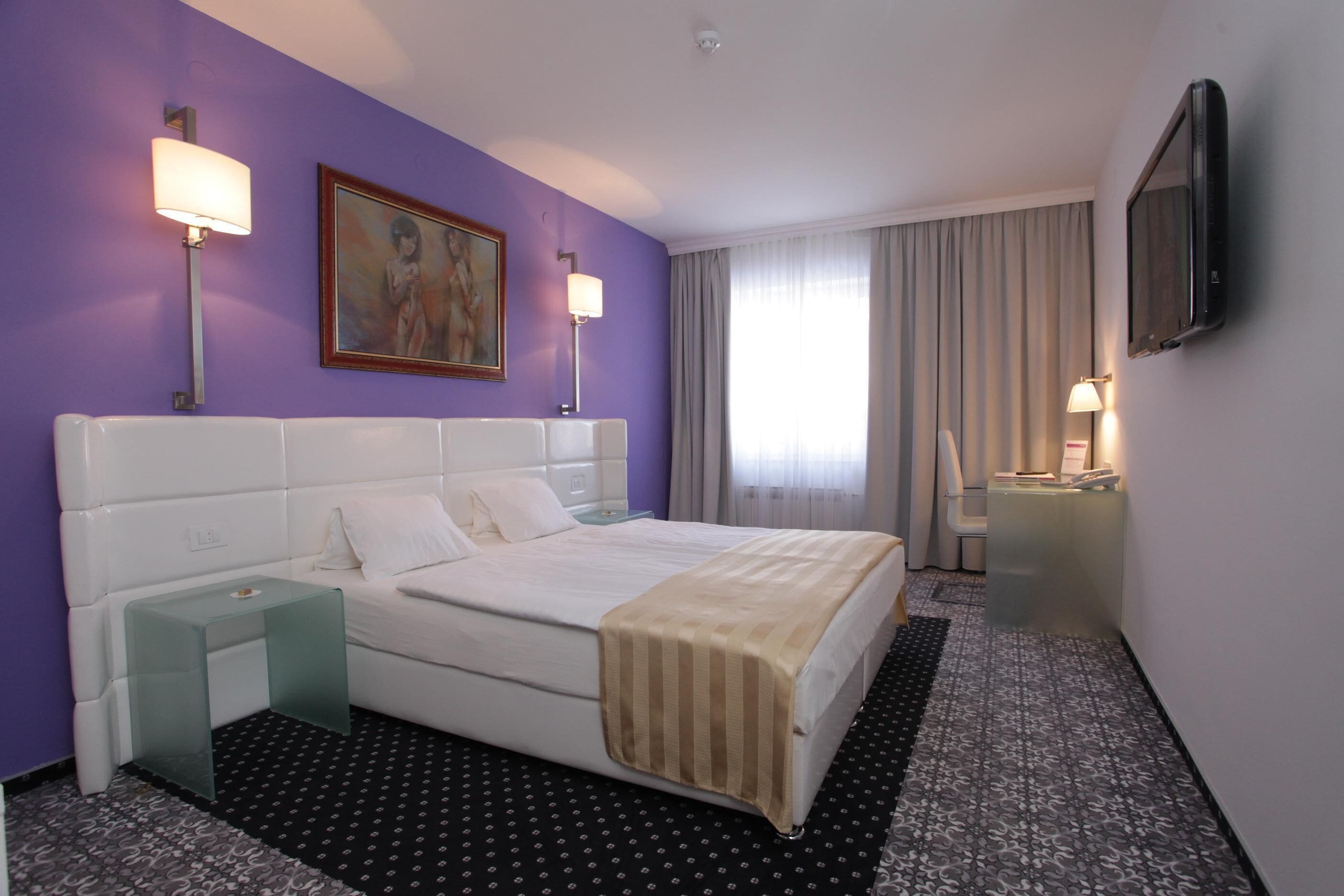 A hotel room with a large bed, two bedside tables, a flat-screen TV, and a painting on the wall.