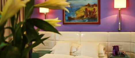 Una habitación de hotel con una cama, dos mesitas de noche, una mesita auxiliar, un cuadro en la pared y una lámpara sobre cada mesita de noche.