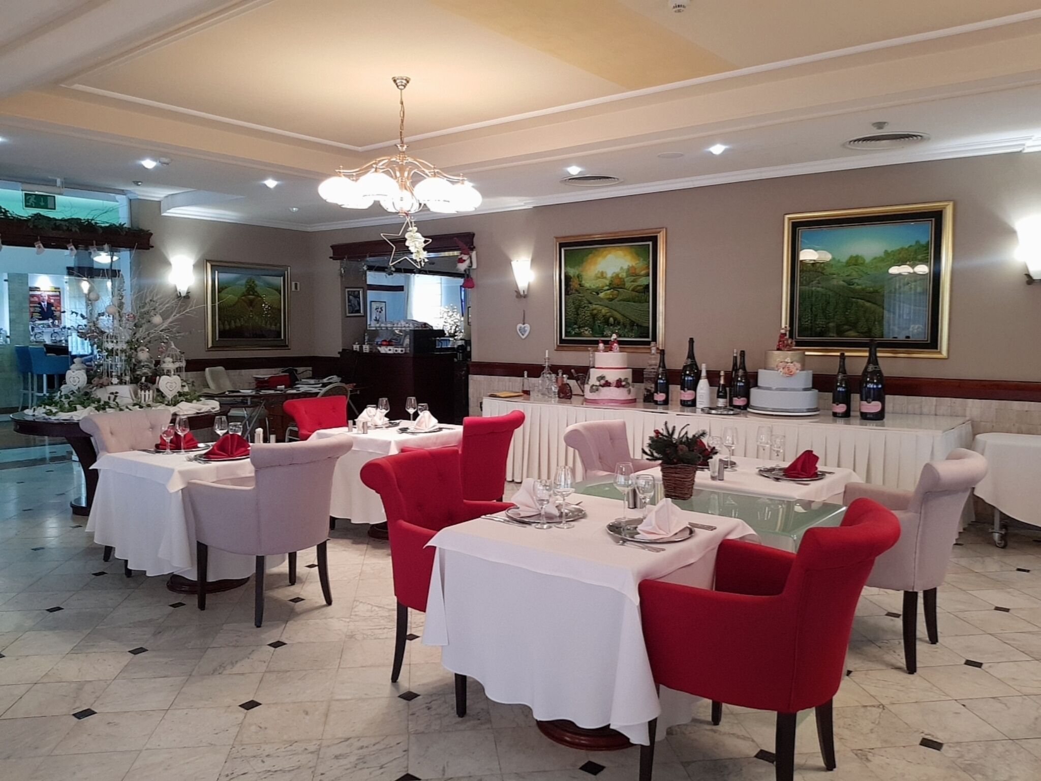 Een restaurant met gedekte tafels, rode stoelen en een kroonluchter.