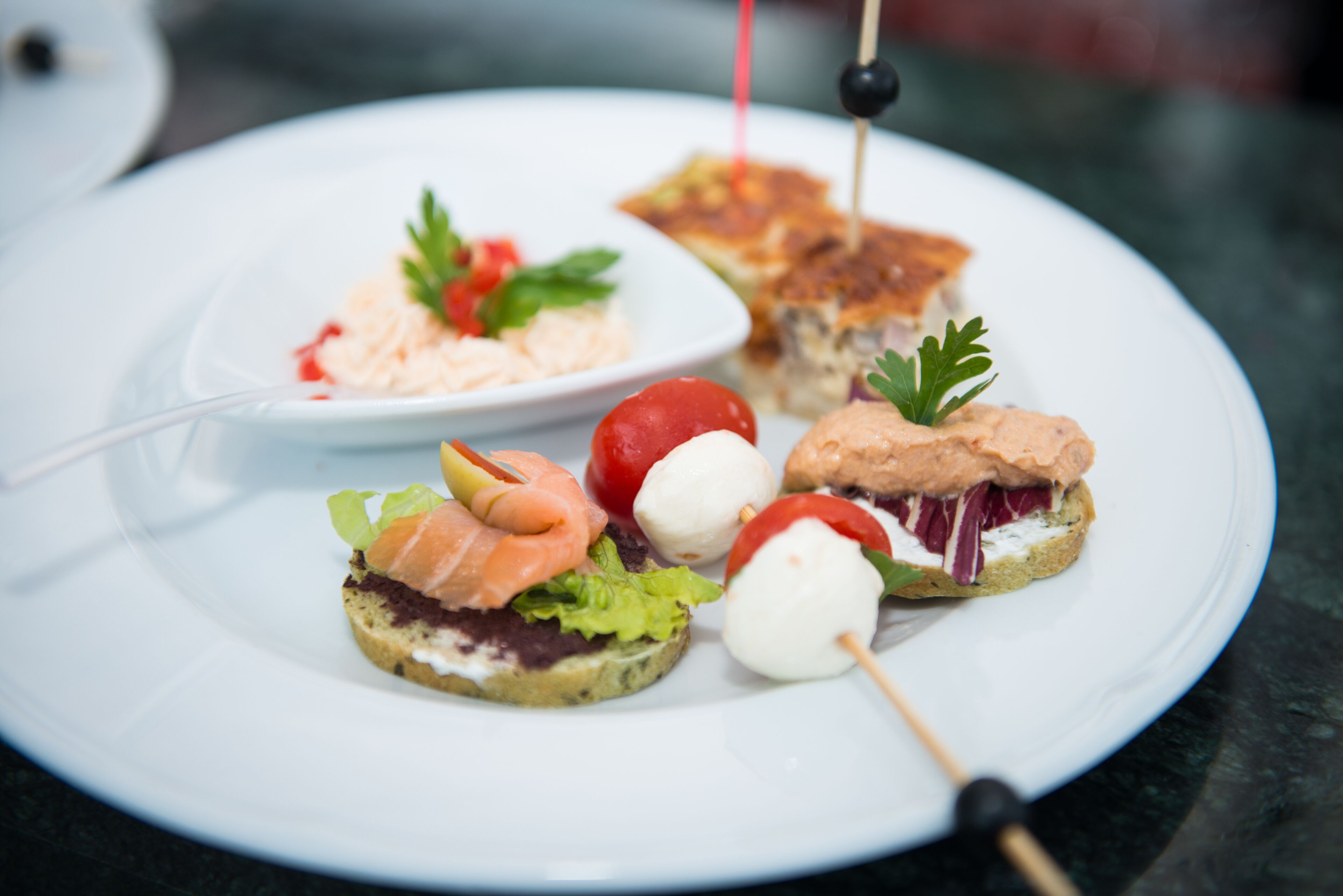 Un plat amb diferents aperitius, com ara un entrepà, un pinxo de mozzarella i tomàquet, i un bol petit amb amanida.