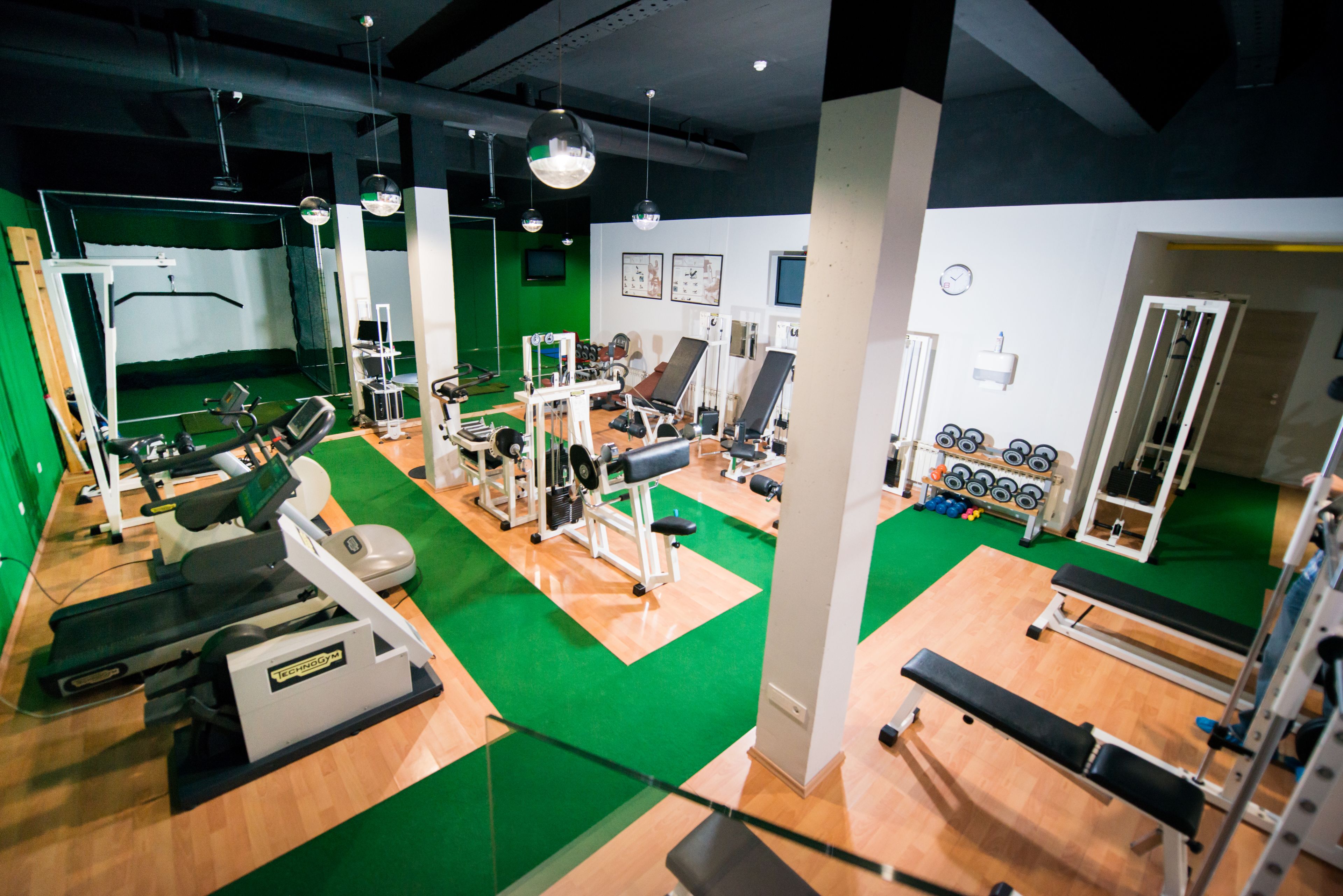 Uma academia com diversos equipamentos de exercício, carpete verde e piso de madeira.