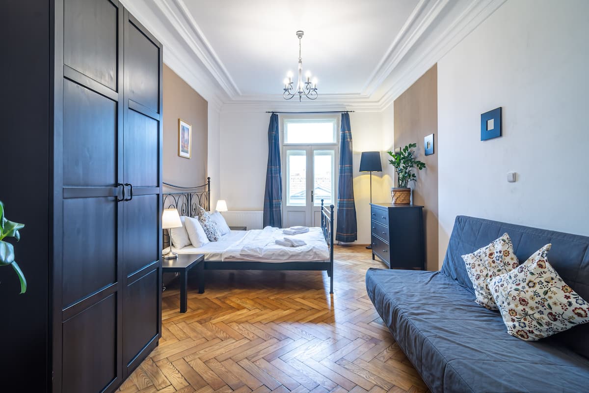 Una camera da letto con un letto, un divano, un armadio, un lampadario e una finestra con tende.