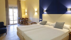 A hotel room with a large bed, a desk, a chair, and a view through a glass door. - Hotel Caribe (Rota)