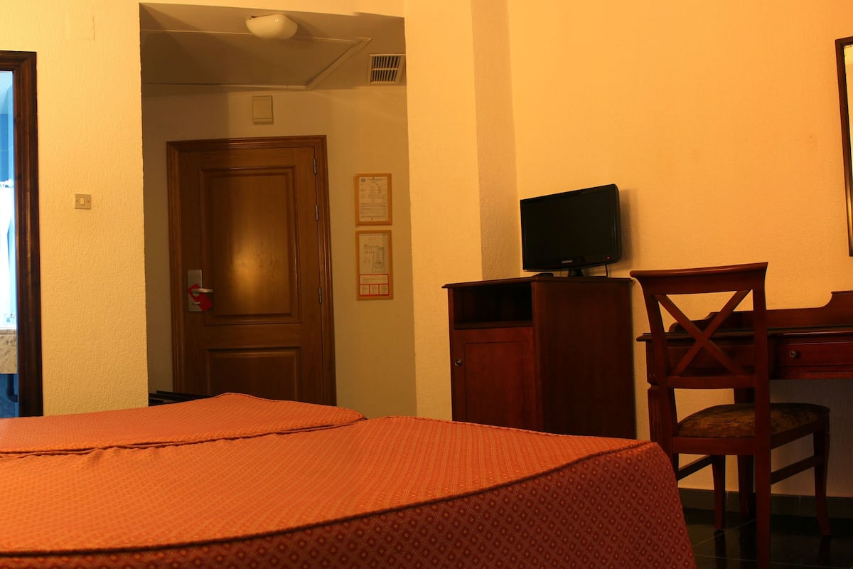 Habitación de hotel con una cama, un escritorio con silla, un televisor y una puerta que da a un baño.