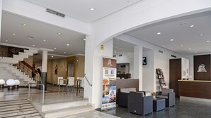 A hotel lobby with a reception desk, seating area, and a staircase leading to another floor. - Hotel Caribe (Rota)