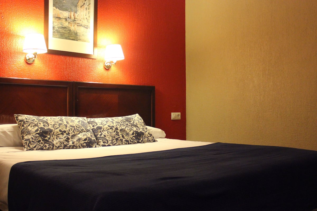 Habitación de hotel con una cama, dos lámparas fijadas a la pared y un cuadro enmarcado sobre la cama.