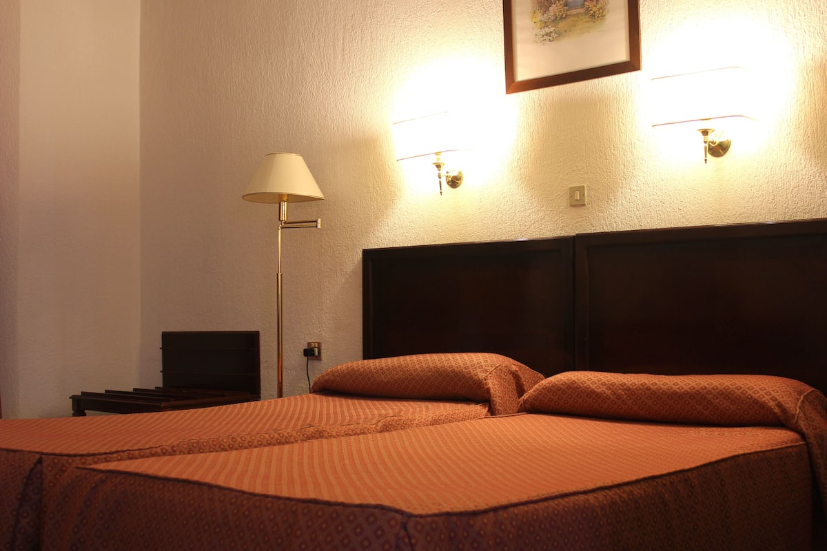 Una habitación de hotel con una cama grande, una lámpara de noche y dos luces empotradas.